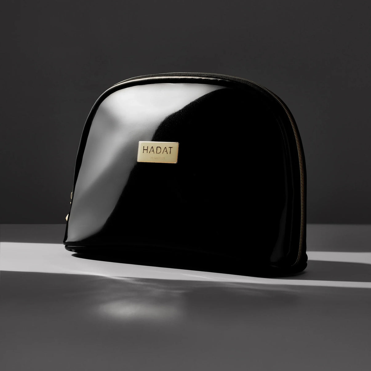 Glossy black Hadat Cosmetics makeup bag with gold logo